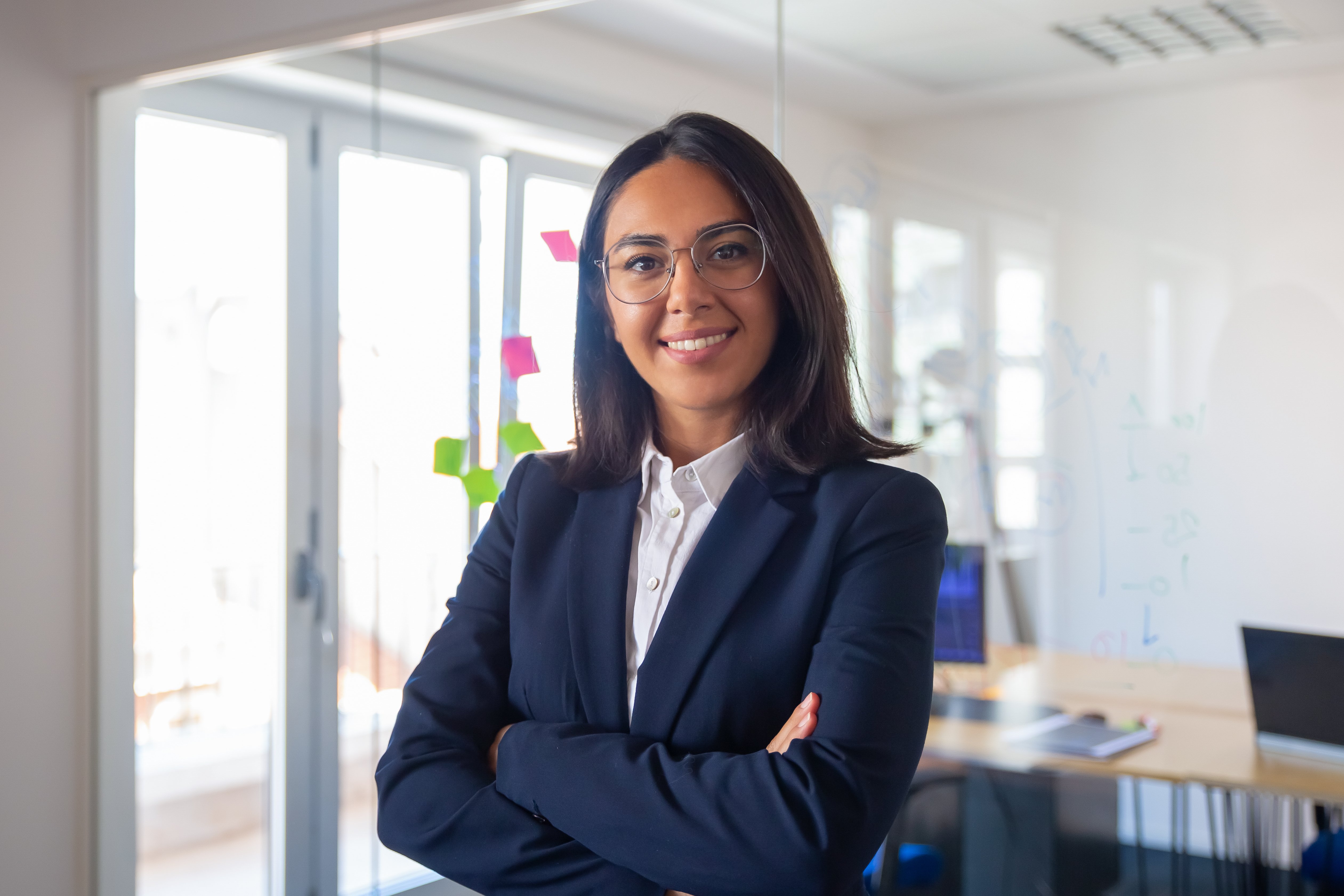 confident-latin-business-leader-portrait-young-businesswoman-in-suit-and-glasses-posing-with-arms-folded-looking-at-camera-and-smiling-female-leadership-concept