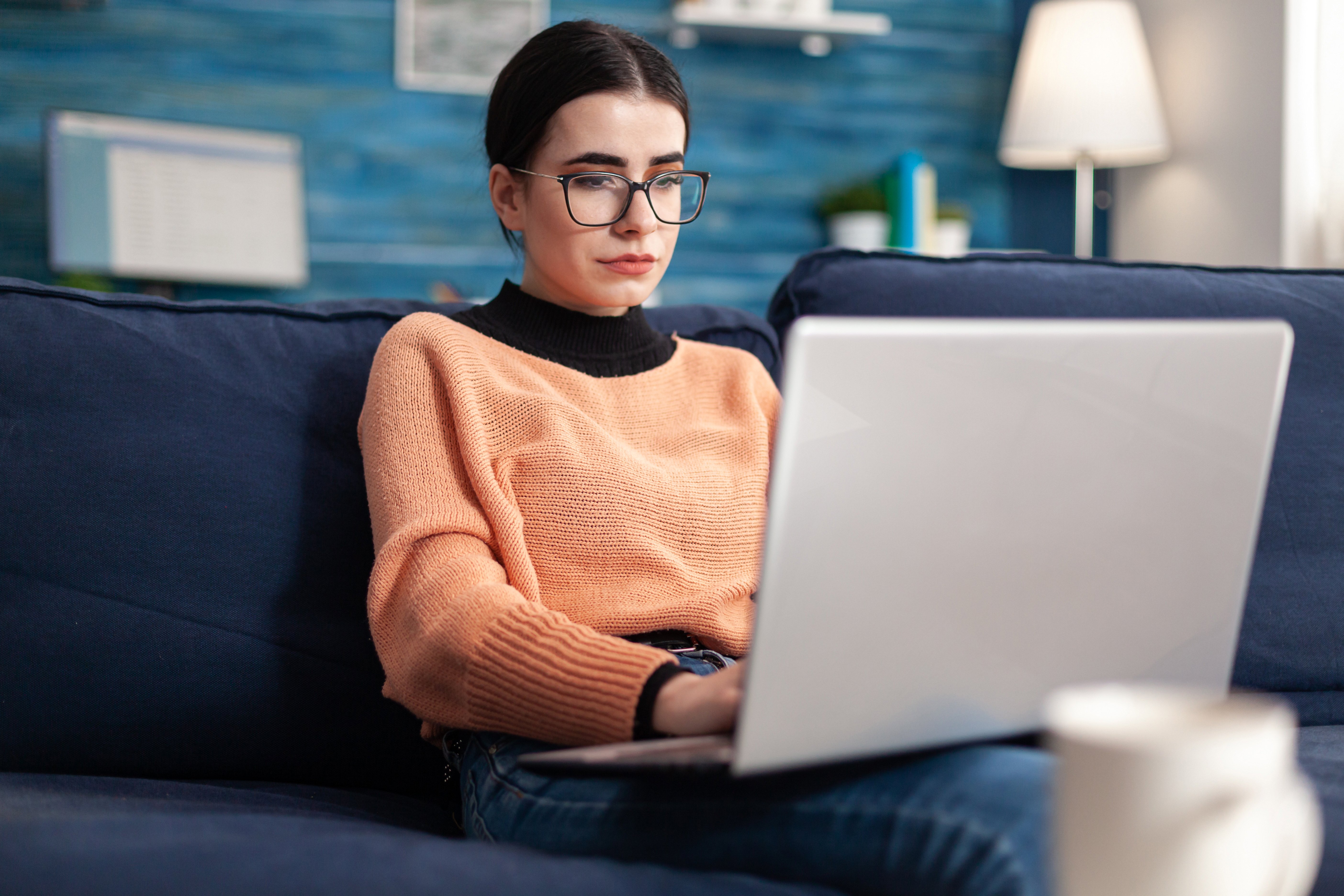 estudante-universitario-de-oculos-verificando-e-mail-no-laptop-enquanto-esta-sentado-no-sofa-da-sala-mulher-estudando-informacoes-de-comercio-usando-a-plataforma-da-universidade-de-e-learning