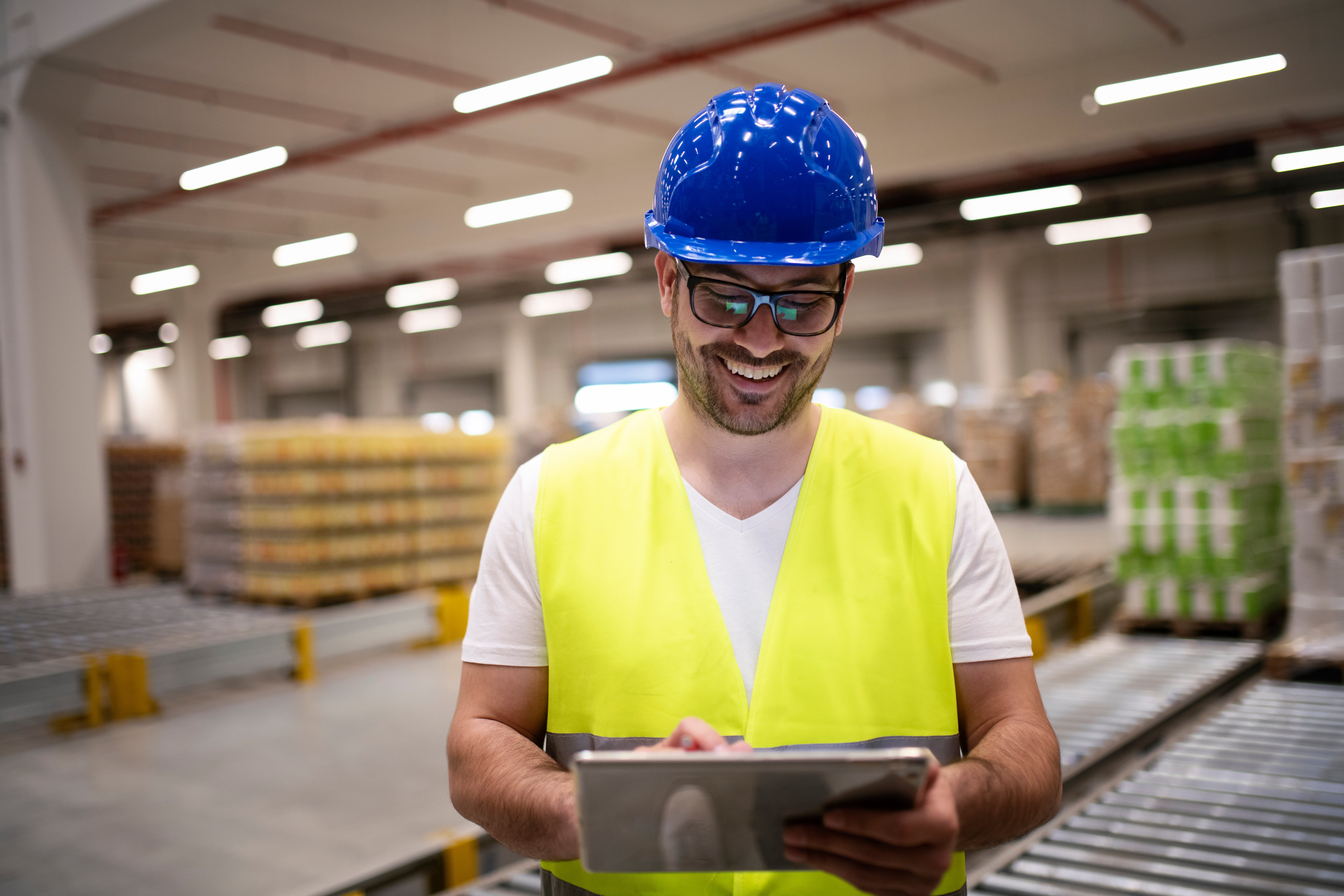 industry-worker-in-reflective-jacket-and-hardhat-looking-at-tablet-in-modern-factory-interior