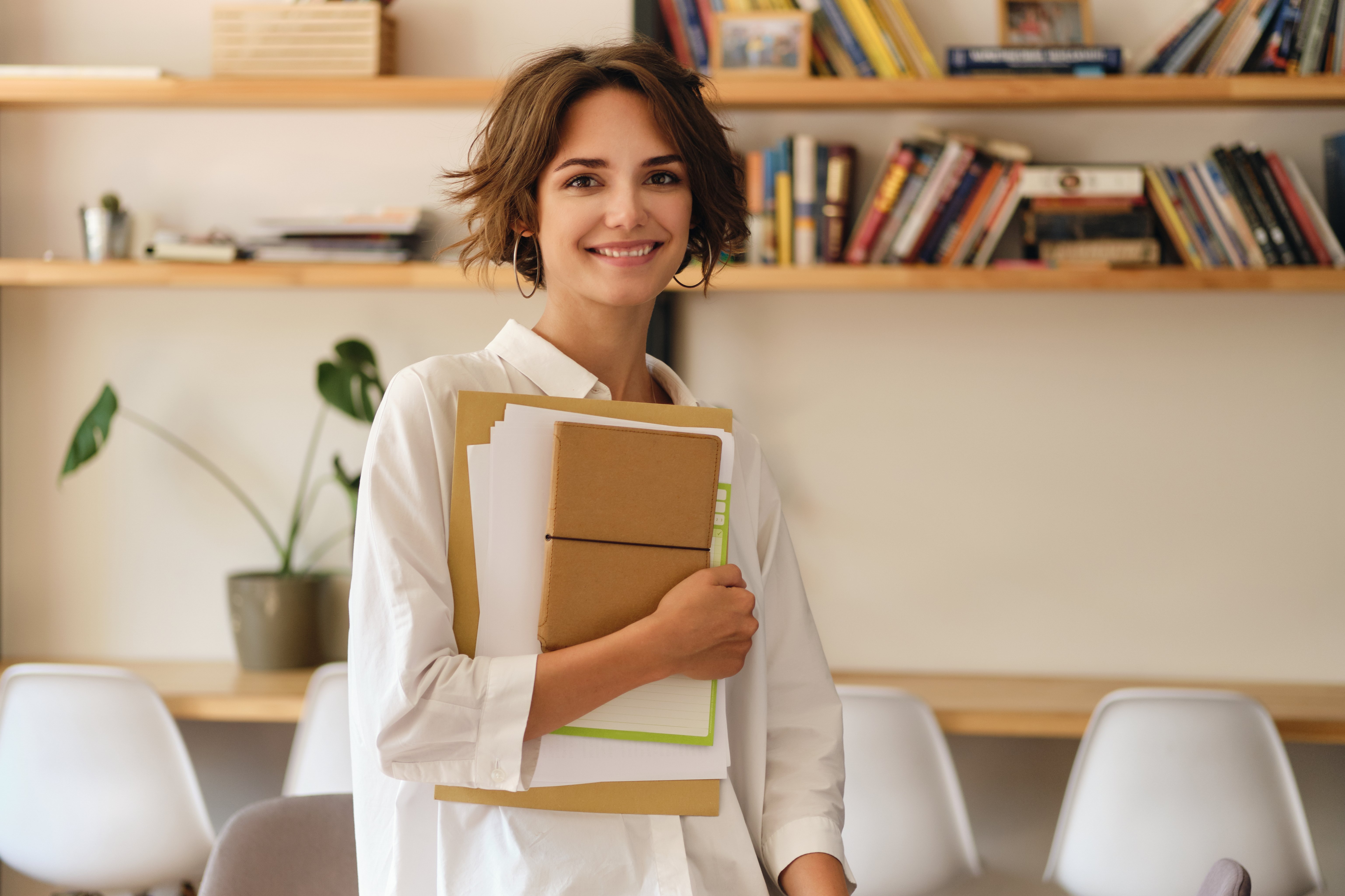 jovem-atraente-sorridente-alegremente-olhando-na-camera-com-papeis-e-bloco-de-notas-no-escritorio-moderno